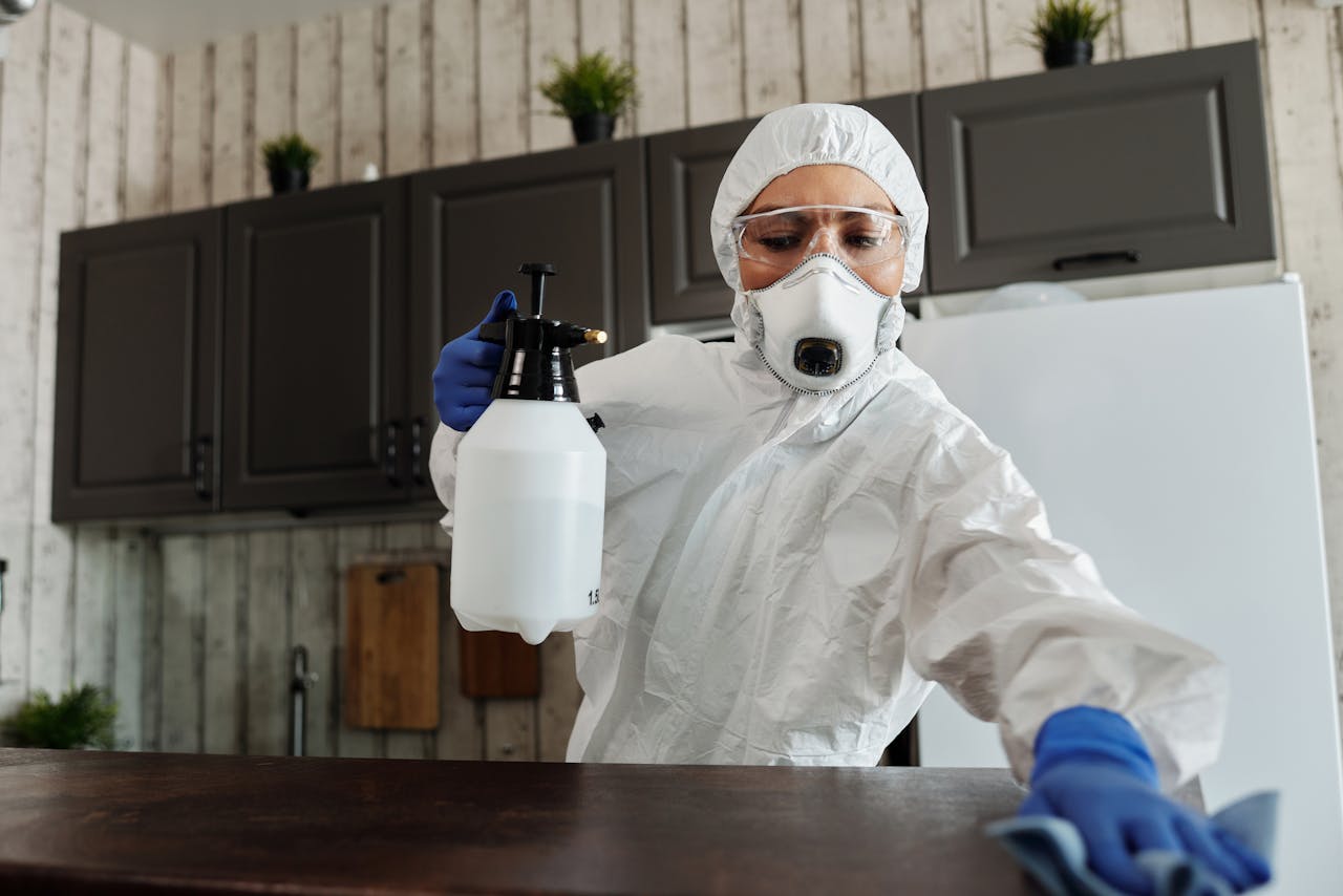 A woman in protective gear disinfecting an indoor area using a spray bottle.